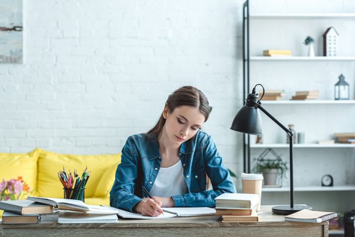concentrated teenage girl writing and studying at desk at home
