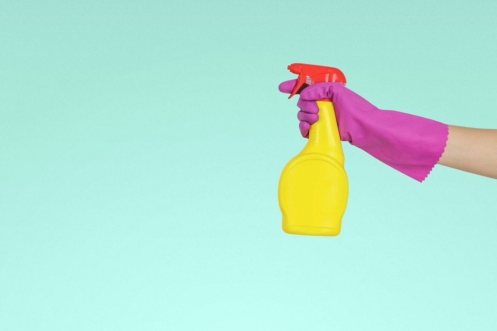 A hand in a pink rubber glove holds a yellow squirt bottle.